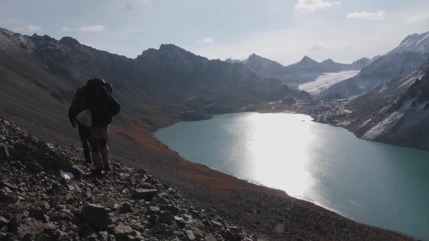 Two people walking amidst a cliff in a mountainous environment with a blue lake