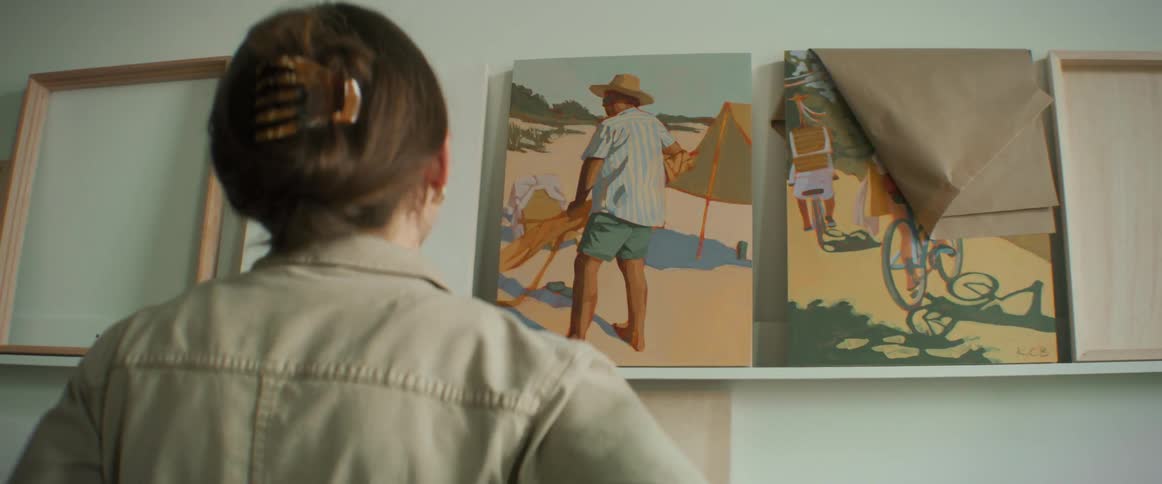 Artist places unframed painting on narrow shelf in an art studio