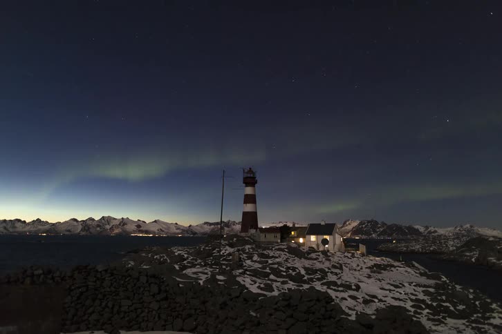 Landscape of a lighthouse amidst lakes and snowy mountains on a day with a timelapse of the northern lights