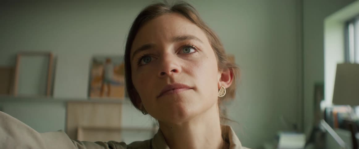 A face of a woman who is doing something with her arm attentively and behind them there are some paintings