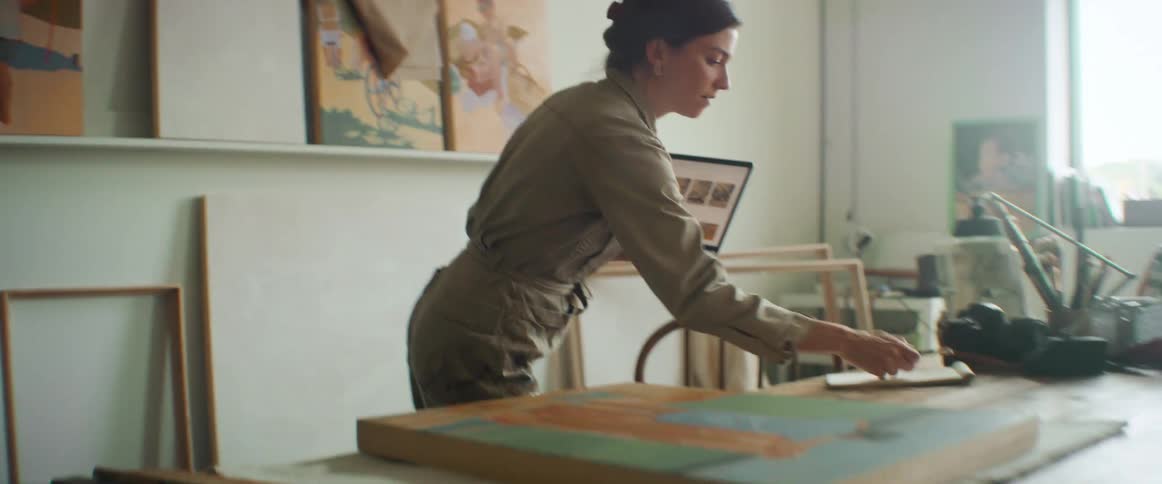 Lady writes on a paper while holding a laptop inside a art studio