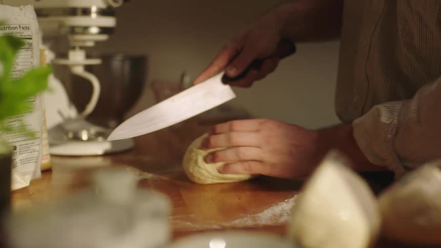 Man wearing a shirt cuts dough with a knife in the kitchen