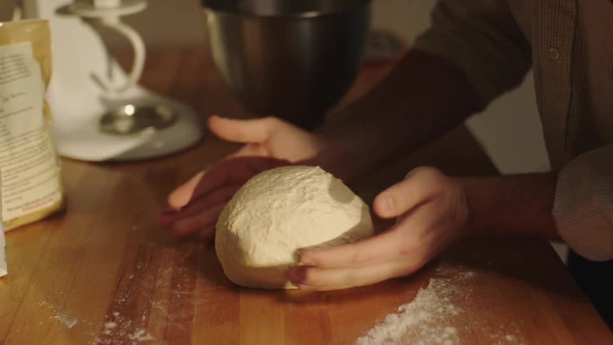 Closeup of a man in a shirt kneading dough with focused determination
