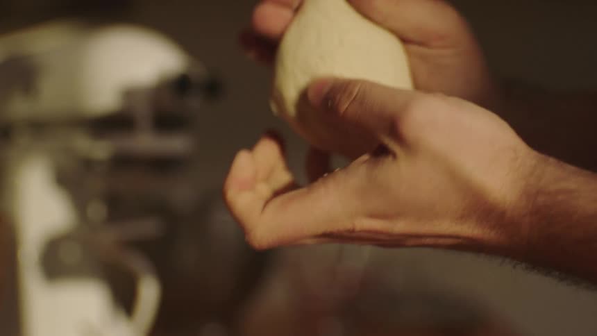 A man kneads and rolls bread dough between his hands
