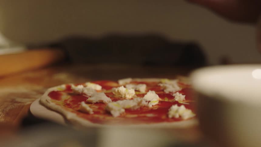 An adult drizzles olive oil over a homemade pizza
