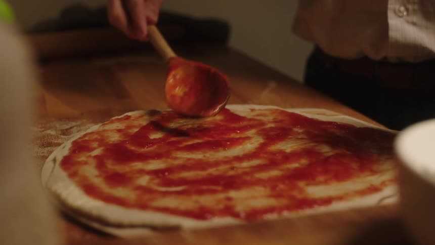 Close up of a man spreading tomato sauce over pizza