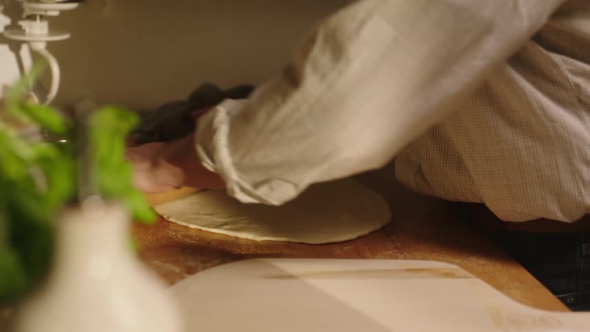 Man rolls pizza dough on wooden counter
