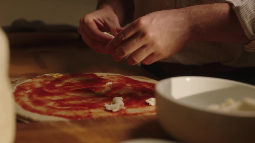 Hands of a person putting ingredients on pizza dough