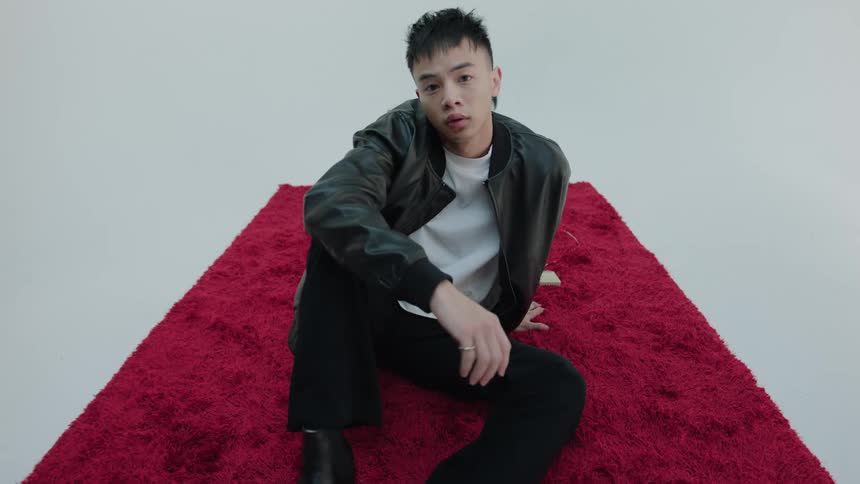 Asian man sitting on a red rug and posing