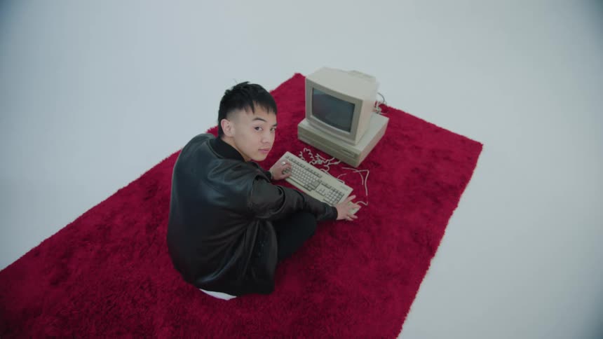 Teenager sits on red rug using an old computer