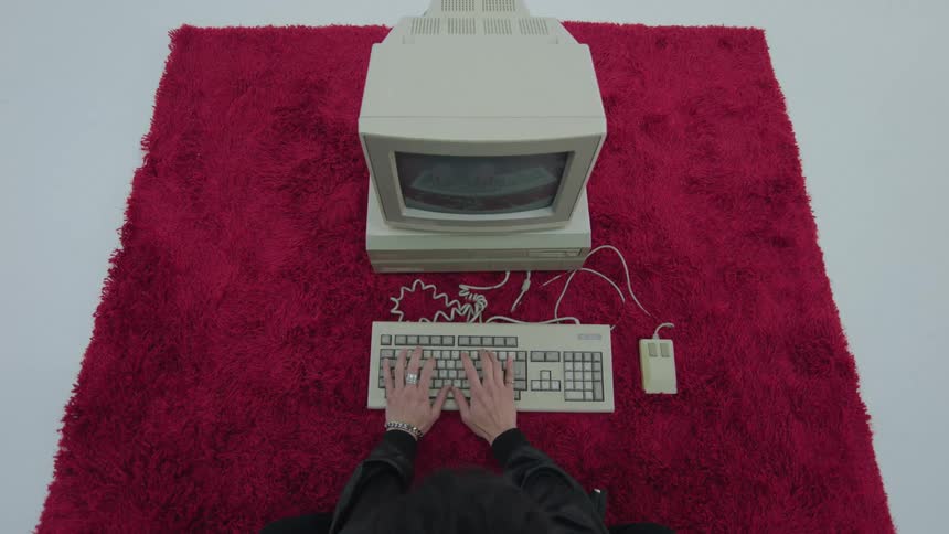 Hands of a person typing on the keyboard of a vintage computer on the floor over a red carpet
