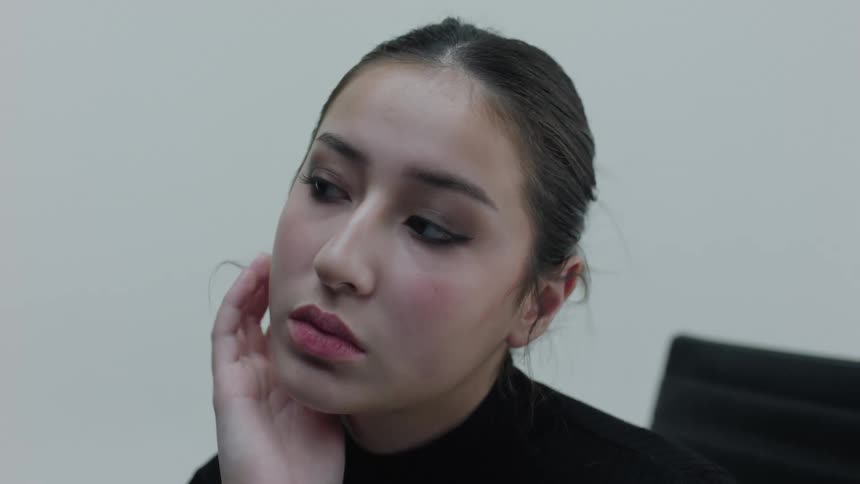 A woman in a black sweater contemplatively thinks in a room