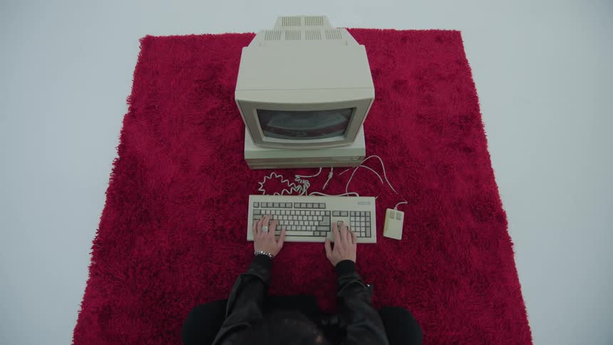 A man sitting on a red rug while typing on a computer