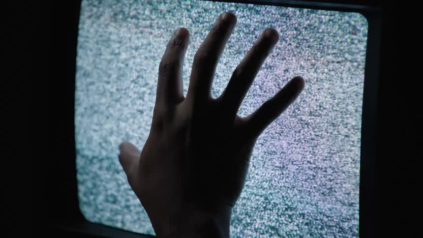 Silhouette of a hand creeping up a screen showing static