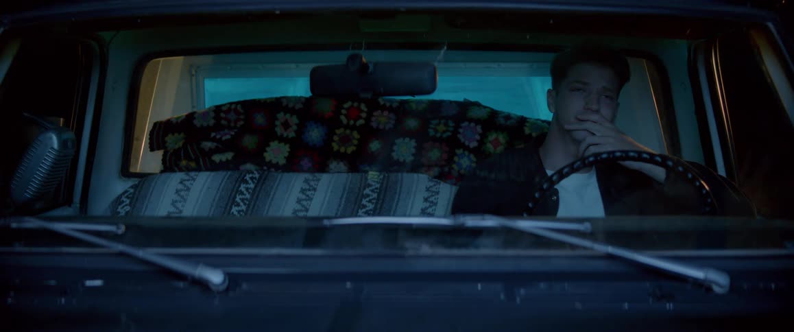 A man is sitting in a stopped car and looking straight ahead with sad expressions