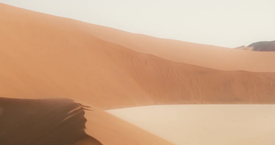 Dusty sand lingers in the air above a large desert sand dune