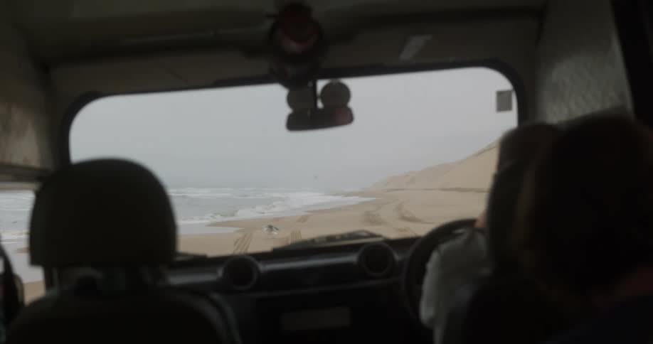 An interior of a car that is driving through sand on a beach