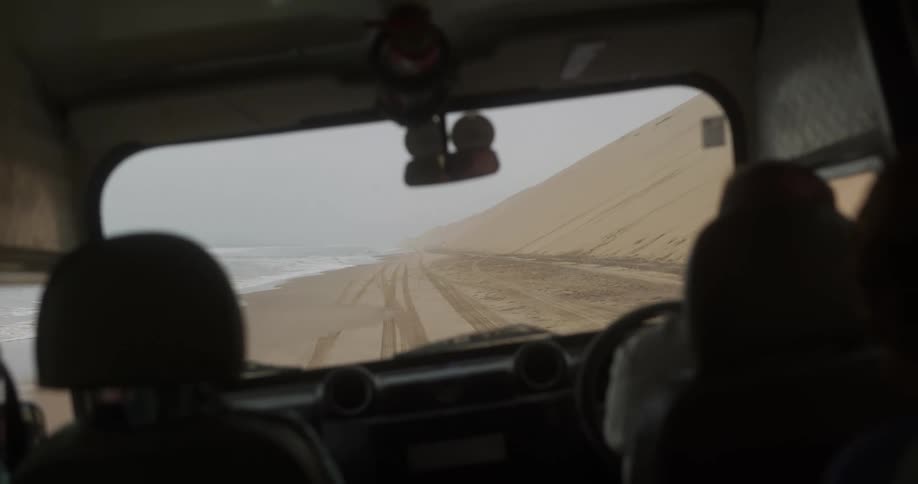 Van driving on a beach next to a sand dune