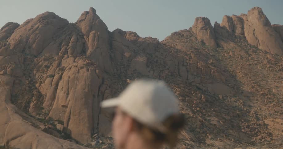 A lady standing in front of a mountain while wearing a white cap