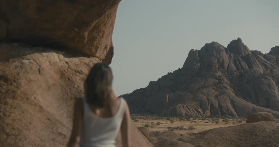 Woman walks under a natural rock arch in the desert next to the mountains