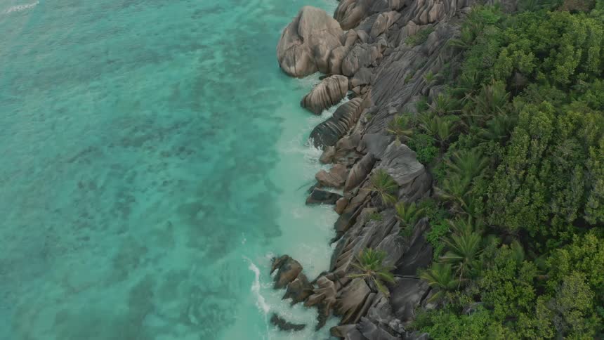 Aerial panorama of the light blue sea crashing against rocks on a paradisiacal coastline