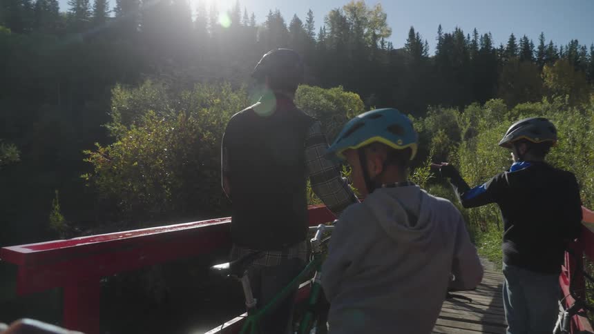 Family of cyclists stands with their bicycles on bridge near woods and looks around