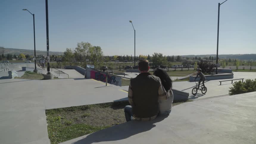 A father and daughter sitting in a city park watching bikers practice