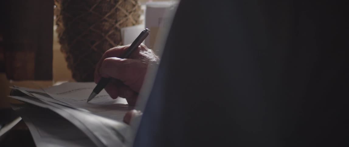 Writing with a pen on the top sheet of a stack of papers at a desk