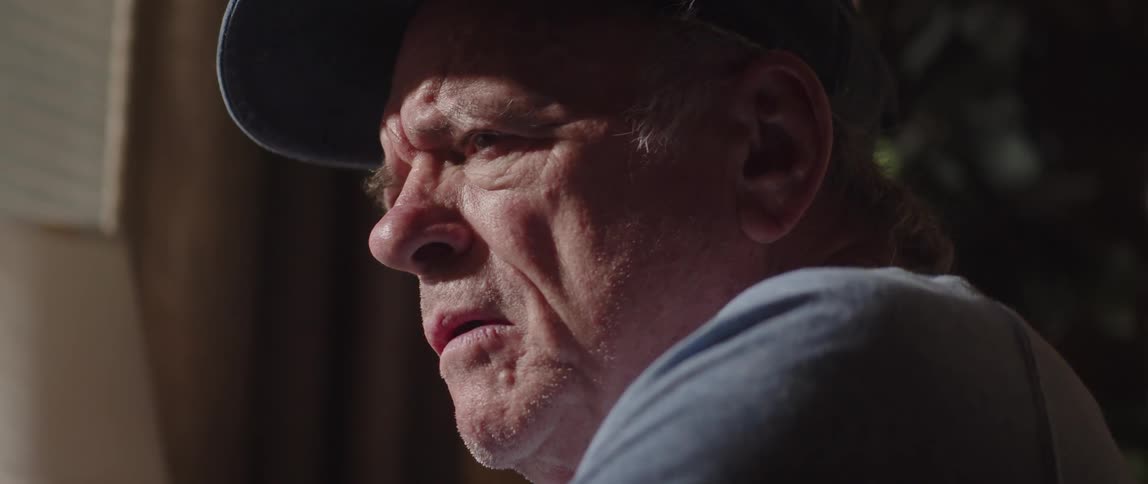 Portrait of an elderly person with a cap indoors putting on their glasses