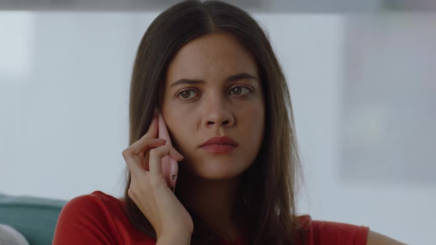 Portrait of a young woman sitting on the couch and on a phone call