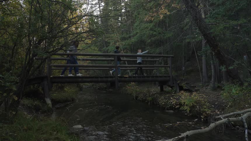A family of four uses a bridge to cross over a river in a forest