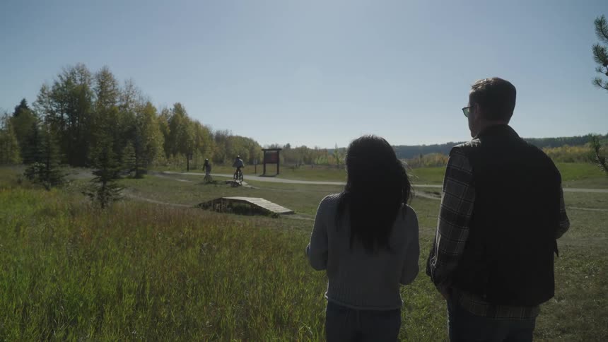 A man and his daughter watch as cyclists go through an obstacle course in a field