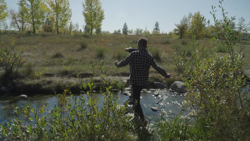 Boys balance on rocks to cross the stream on a sunny day