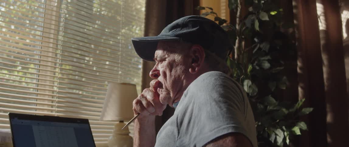 Elderly man sitting in a chair in front of his laptop looking thoughtful