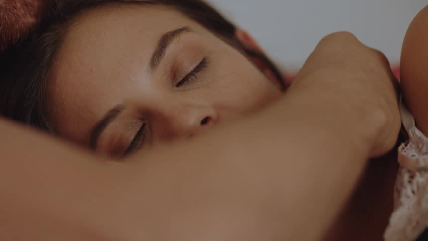 A woman has a man in a mans lap as theyre both lying down and he caresses her face while she touches his arm