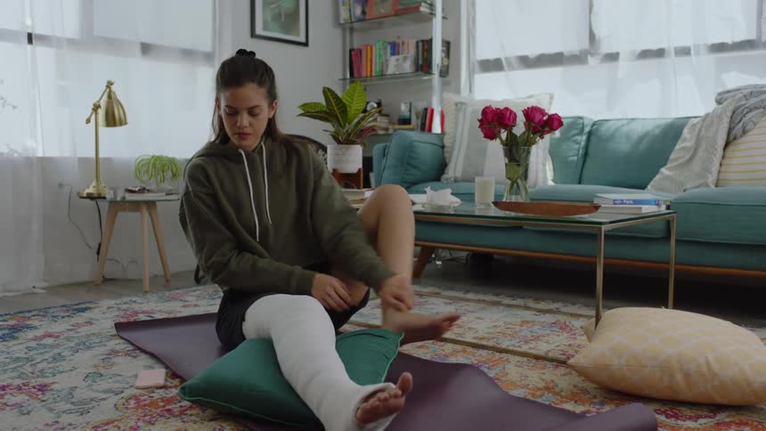 Woman with one leg in a cast sitting on the ground massaging her other leg