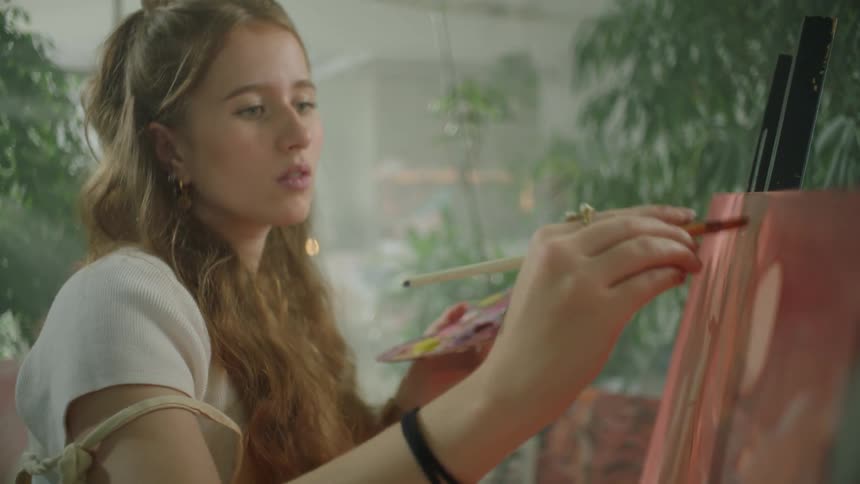 A young girl is painting a canvas with a brush and its very focused