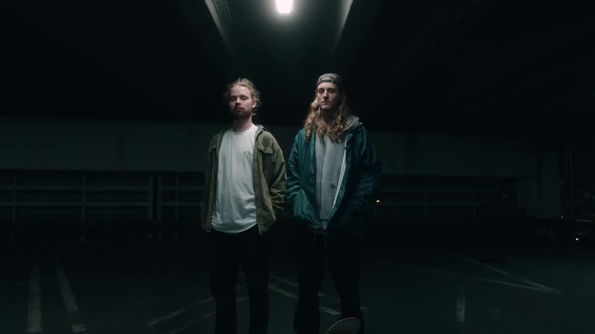 Two men are standing in the dark under a spotlight