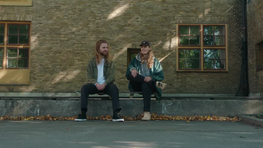 Two men chat while sitting on a ledge outside