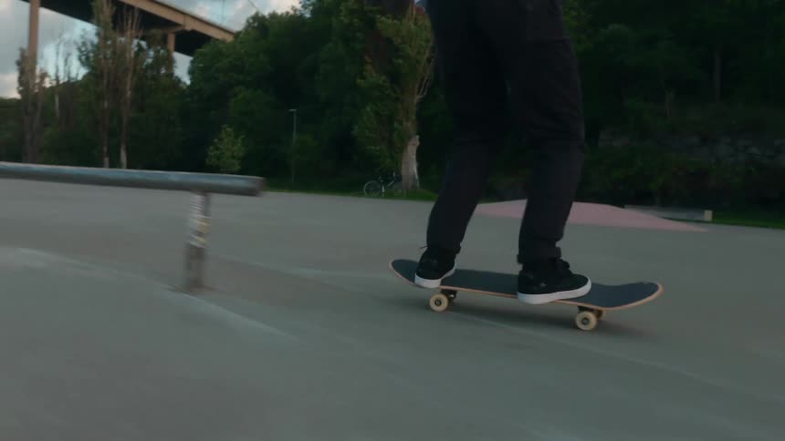 Male skateboarder with bun beard green jacket and jeans rides skateboard and jumps over bench in the park