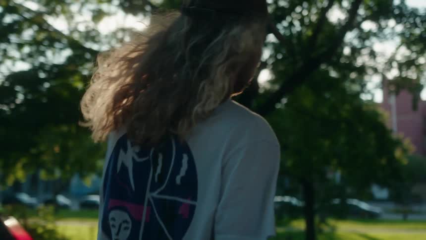 Young man with long hair rides a skateboard on the city street at evening