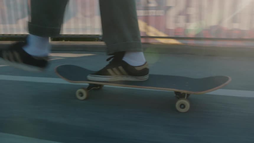 A young man skateboards across a pedestrian bridge over a highway toward a park