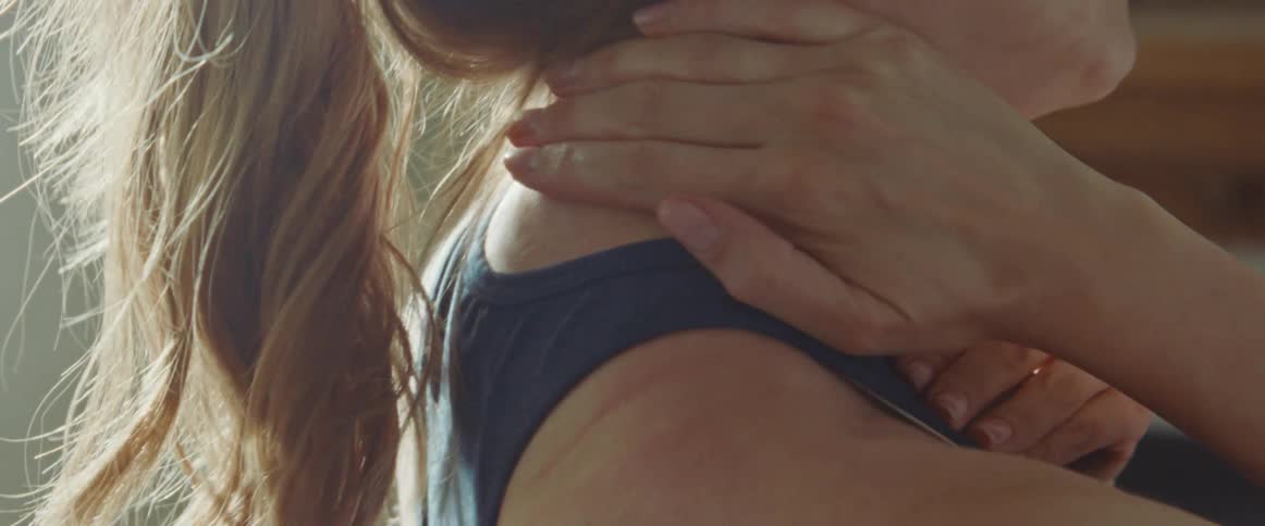 Woman with a ponytail and a sport top rubs her back and neck after workout in the living room at home