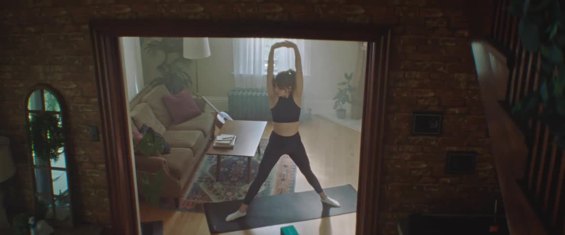 Pregnant woman with a ponytail sport top and leggings does stretching on a pilates mat in the living room at home