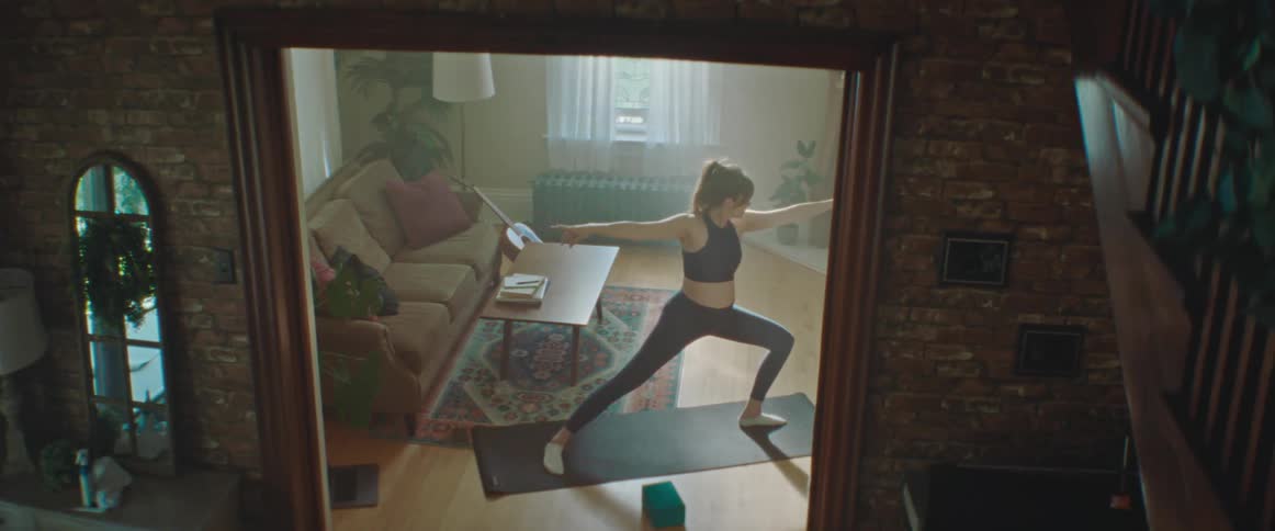 Pregnant woman with a ponytail sport top and leggings works out on a pilates mat in the living room at home