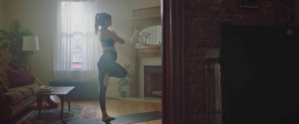 Pregnant woman with a ponytail sport top and leggings exercises on a pilates mat in the living room at home