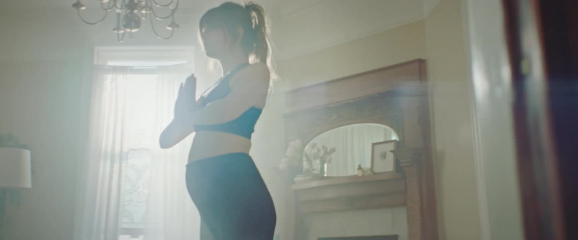 Pregnant woman with a ponytail sport top and leggings exercises on a pilates mat in the living room at home