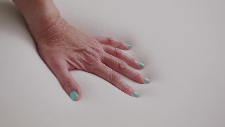 Hand with painted nails leaves imprint on soft memory foam mattress