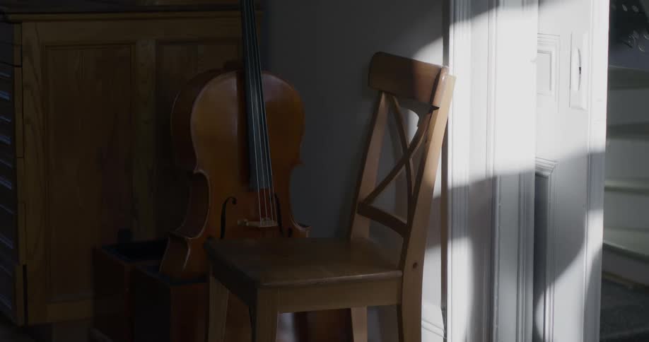 Double bass sits behind a wooden chair near a doorway with sunlight just reaching the top