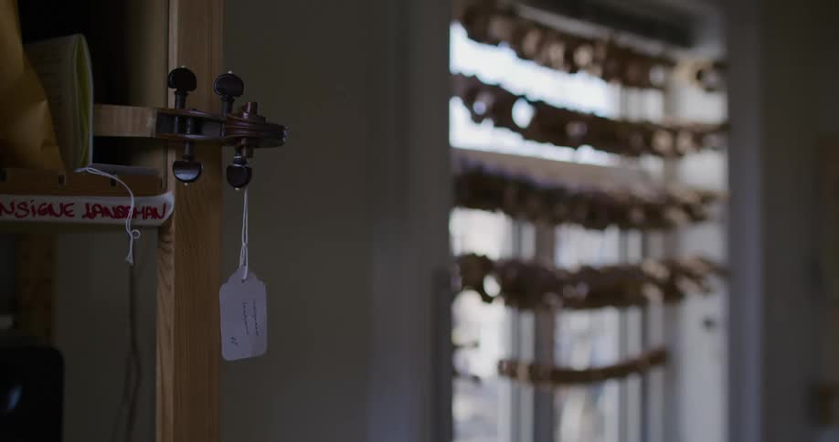 A violin with a tag dangling from it as it sits on a shelf in a workshop